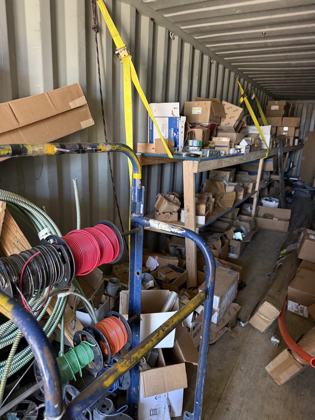 Inside a job-site Conex: wire spools on a cart, shelves of fittings boxes