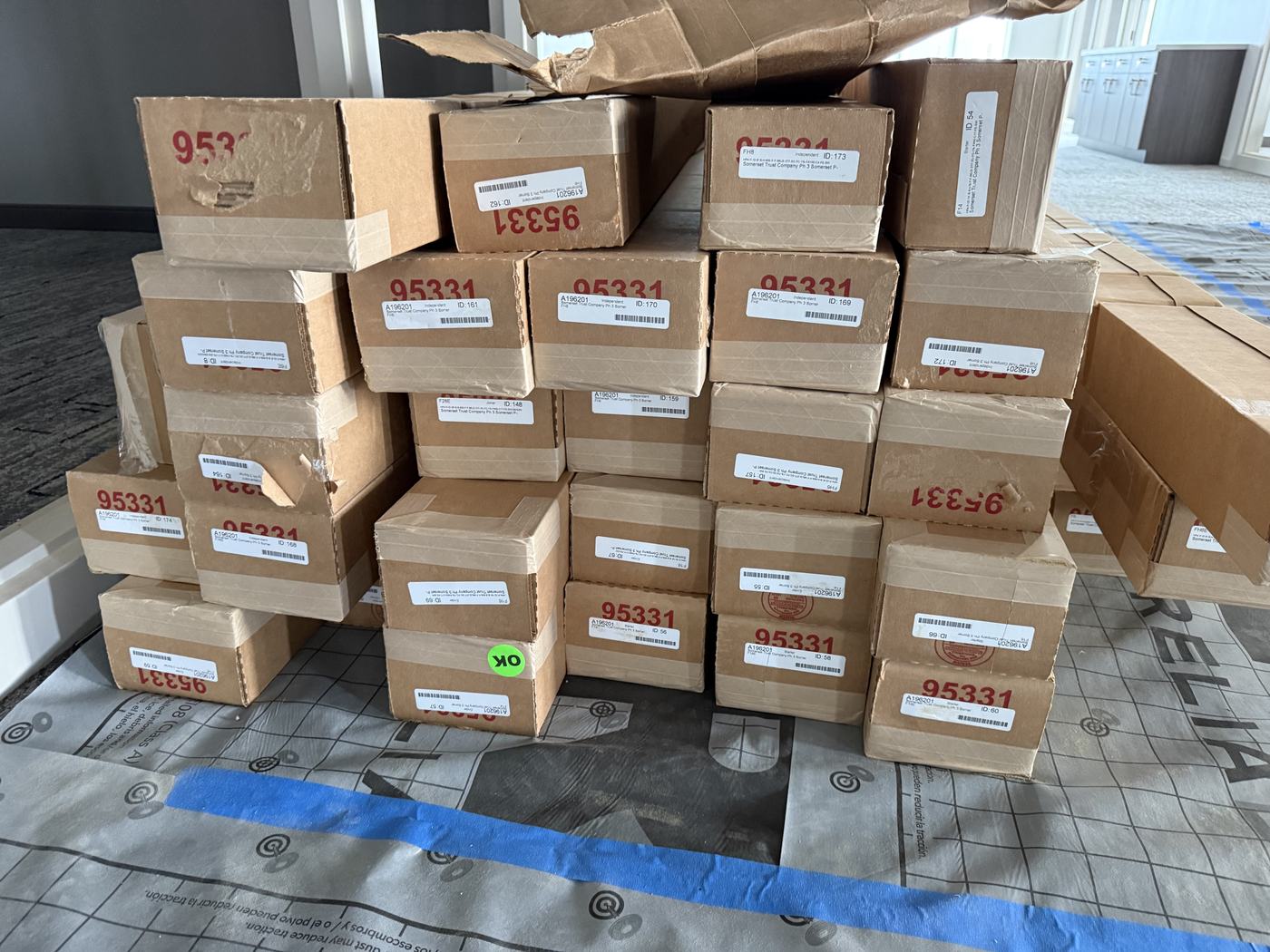 Dozens of light fixture boxes for one job stacked on floor protection